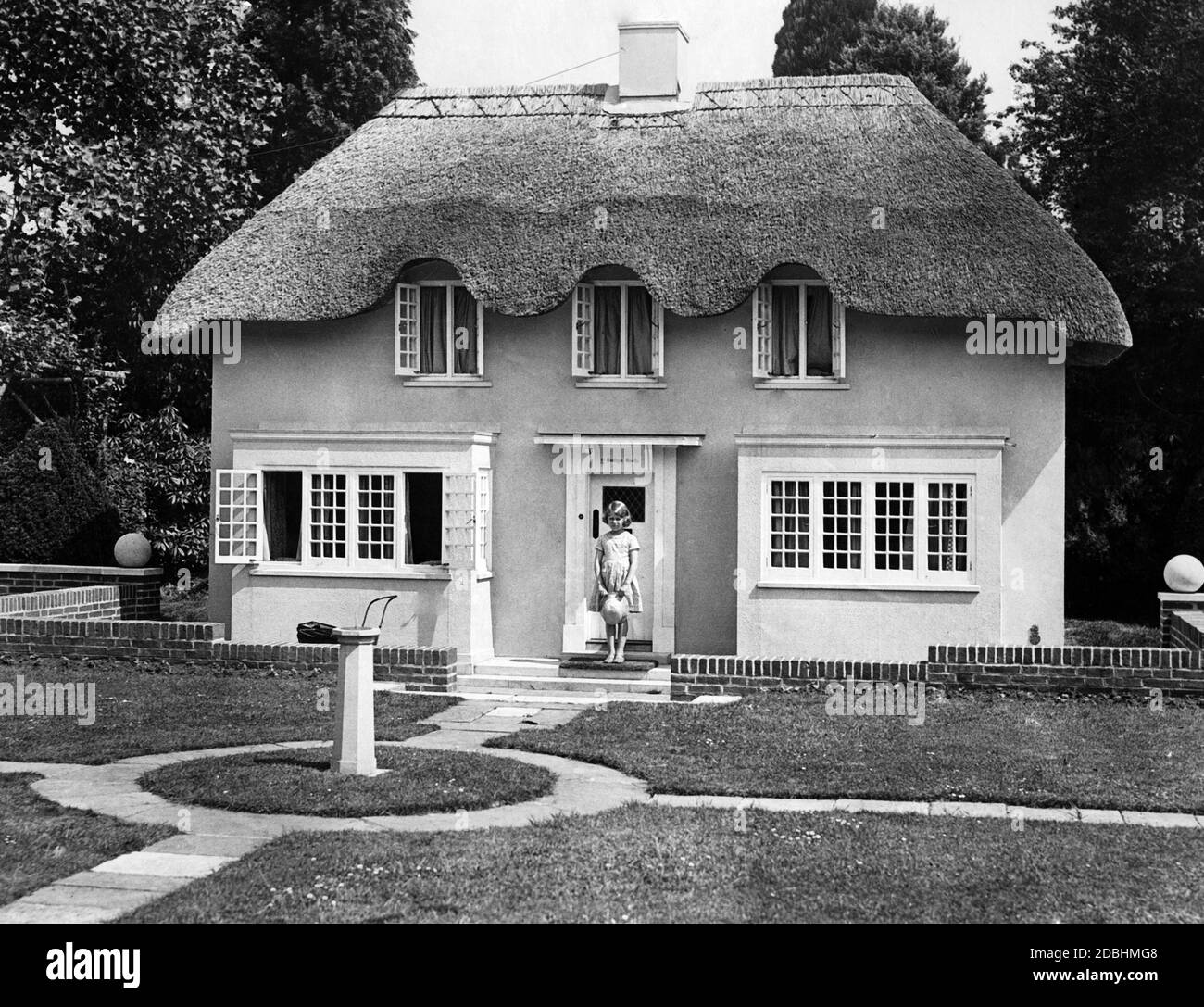 Elizabeth II steht vor einem Modellhaus, das im Stil eines alten walisischen Landhauses in Größe 2/5 gebaut wurde. Dies war ein Geschenk an Prinzessin Elizabeth zu ihrem 6. Geburtstag von den Walisern. Das Haus verfügt über Gas, Wasser, Telefon und elektrisches Licht und wurde von Herrn Morgan Willmott, F.R.I.B.A. von Cardiff entworfen. Durch die öffentliche Darstellung des Hauses wird Geld für wohltätige Zwecke gesammelt. Stockfoto