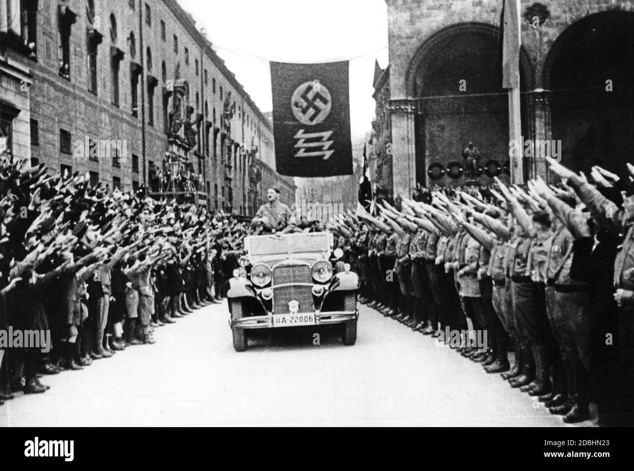 "Adolf Hitler und die NSDAP feiern die Erreichung ihrer Ziele am 9. November 1933, 10 Jahre nach dem gescheiterten Putsch. Hitler war in diesem Jahr Reichskanzler geworden. An der Stelle unter der Flagge mit Hakenkreuz und Wolfsangel, die im Hintergrund zu sehen ist, wurde eine Gedenktafel zu Ehren der Märtyrer vom 9. November 1923 angebracht, die nur durch das Angrüßen mit dem Nazi-Gruß übergeben werden konnte. Ab diesem Zeitpunkt wurde der 9. November zum nationalsozialistischen Feiertag, in dessen Rahmen der traditionelle marsch vom Bürgerbraeukeller am Wiener Platz über die Ludwigsbrücke stattfand Stockfoto
