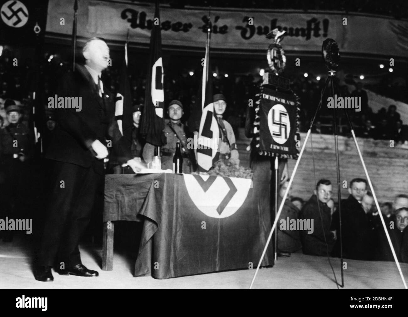 Hitler während einer Rede im Sportpalast. Nach seiner Inhaftierung in Landsberg wurde ihm drei Jahre lang das öffentliche Sprechen untersagt. Auf einem Banner stehen die Worte "Unser die Zukunft". Stockfoto