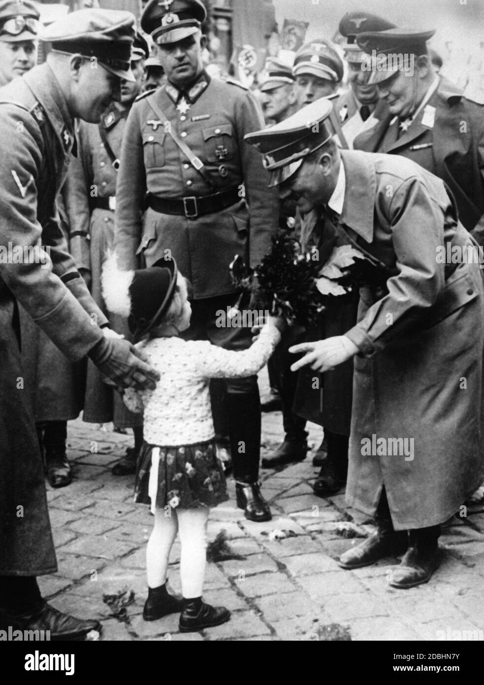 Adolf Hitler, der mit Begeisterung aufgenommen wird, wird von einem kleinen Mädchen mit Blumen überreicht, als die Wehrmacht das Sudetenland einmarschiert. Hermann Göring steht hinter Hitler. Stockfoto