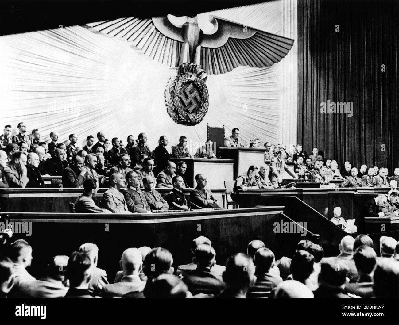 Adolf Hitler während seiner Rede über die Kriegserklärung an die USA. Links von Hitler sind Julius Schaub und Hans Heinrich Lammert, rechts Otto Dietrich und Albert Bormann. Über ihm, Reichstagspräsident Hermann Göring. Neben Hitlers freiem Sitz auf der Regierungsbank sind Joachim von Ribbentrop, Erich Raeder, Walther von Brauchitsch, Wilhelm Keitel, Wilhelm Frick und Joseph Goebbels. Auf der Bank oben, von rechts sitzend: Johann Ludwig Graf Scherin von Krosigk, Walther Funk, Walter Darre, Bernhard Rust, Hanns Kerrl, Hans Frank, Julius Dorpmueller, Arthur Seys Inquart und Fritz Todt. Stockfoto