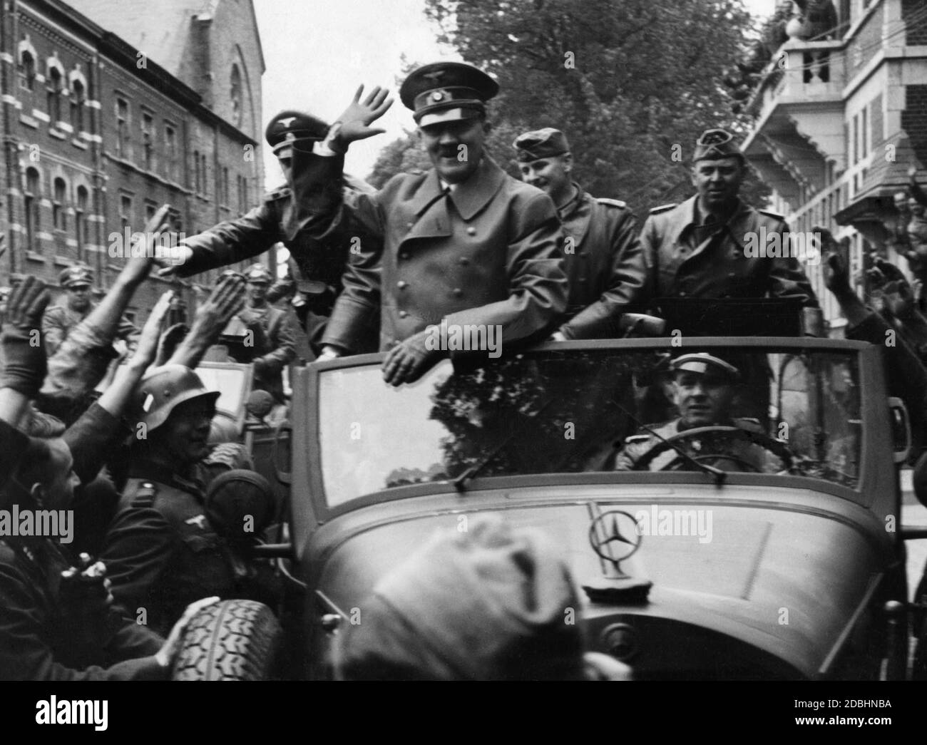Adolf Hitler wird von seinem Fahrer Erich Kempka durch eine Stadt in Ostfrankreich gefahren. Rund um den Mercedes W31 begrüßen ihn Angehörige der Wehrmacht. Rechts von Hitler ist sein Adjutant Julius Schaub. Stockfoto