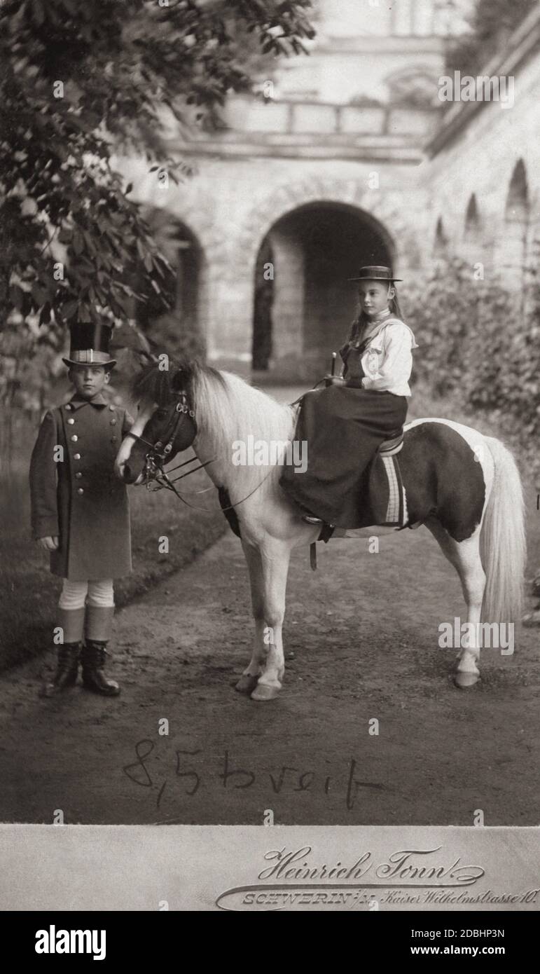 Cecilie von Mecklenburg sitzt in einem Seitensattel auf einem Pony, das von einem Jungen mit Zylinderhut gehalten wird. Foto von Heinrich Tonn, einem Schweriner Fotografen. Stockfoto