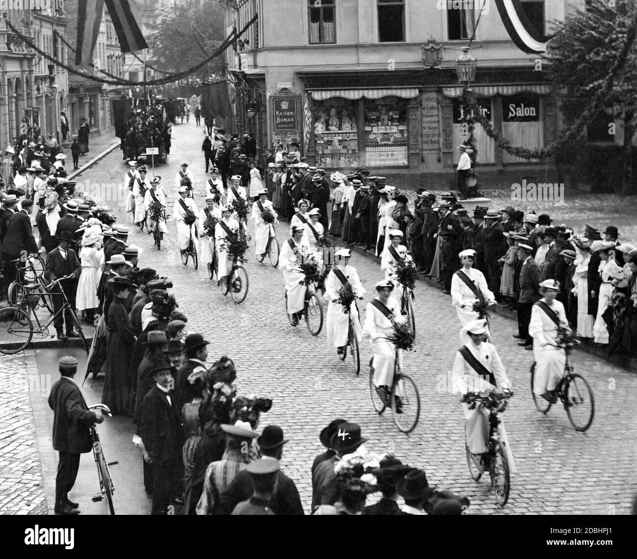 In weiß gekleidete Ehrenmädchen auf Fahrrädern in einer Parade zu Ehren eines Radsportclubs in einer kleinen deutschen Stadt. Stockfoto