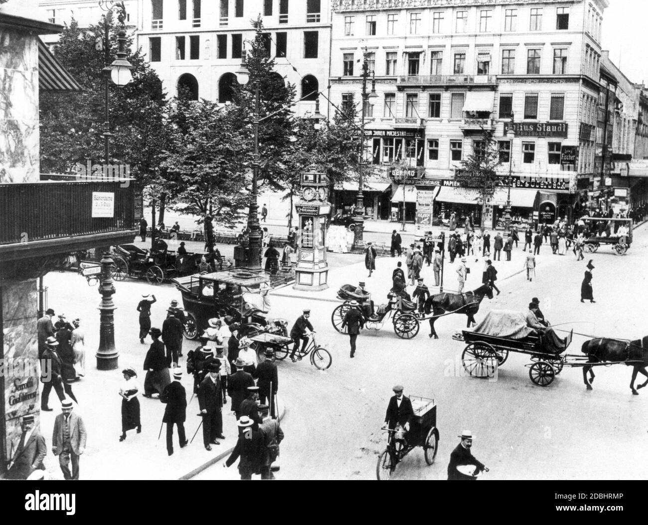 'Das Foto zeigt die Kreuzung Friedrichstraße und unter den Linden in Berlin 1913, gefüllt mit Karren und Passanten, mit zahlreichen Plakaten, die an den Häusern hängen, darunter eine mitten in der Straße:''Julius Staudt. Photograph'', ''Ludwig Fischer'' und ''Krueger & Oberbeck'' (Tabakladen). Stockfoto