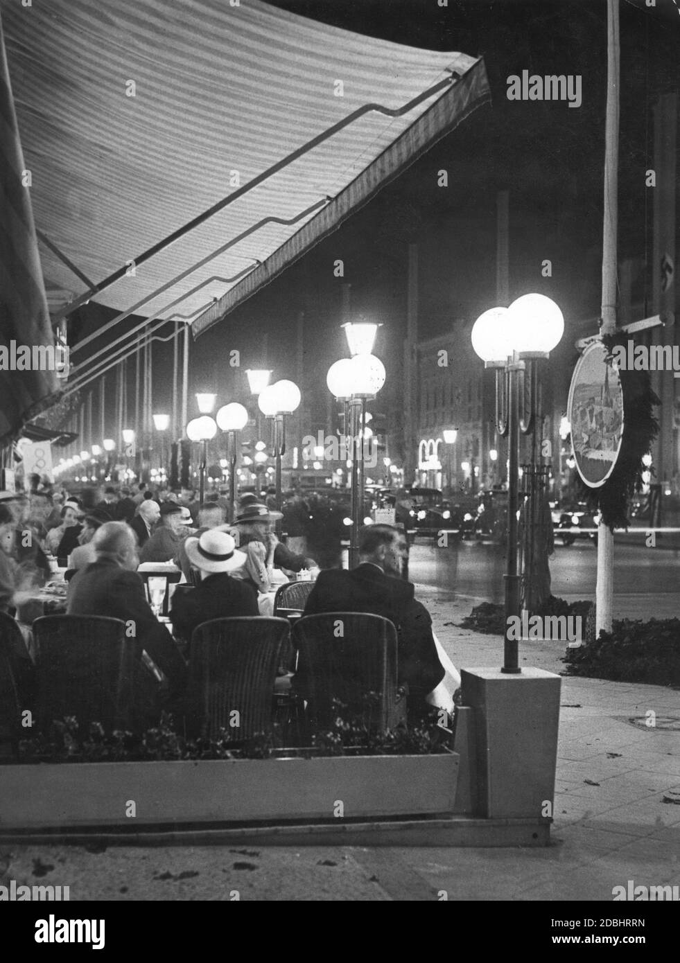 Die Gäste des Berliner Cafés sitzen an einem Sommerabend im Jahr der Olympischen Spiele 1936 draußen und beobachten den Verkehr auf dem Boulevard unter den Linden. Stockfoto