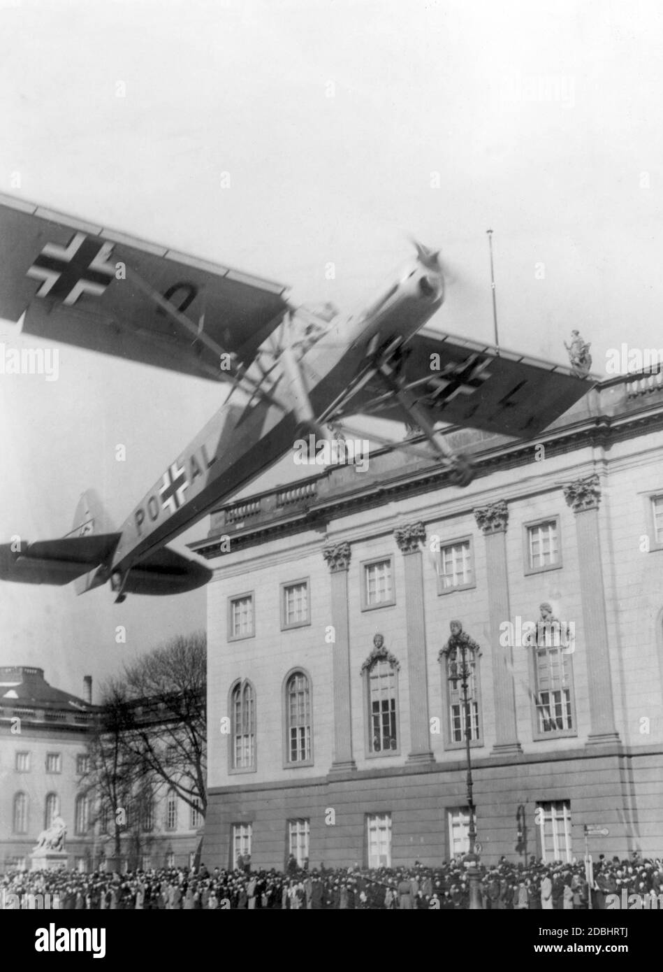 'Das Flugzeug ''Fieseler Storch FI 156'' konnte besonders langsam fliegen. Hier geht es am Tag der Wehrmacht in Berlin am 17. März 1940 von der Straße unter den Linden aus. Eine Menschenmenge vor der Humboldt-Universität schaut von der Seite der Straße." Stockfoto