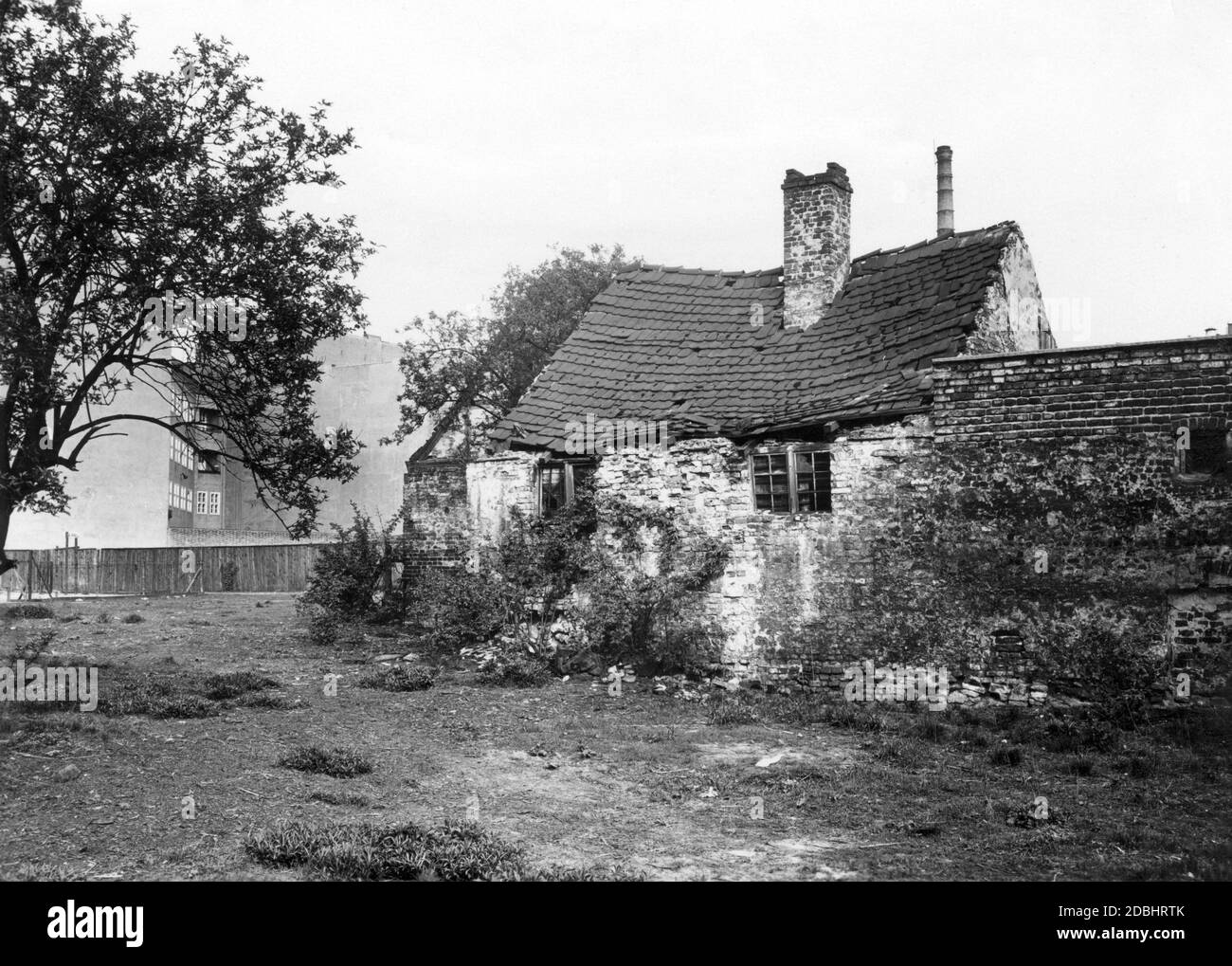 Das Foto von 1932 zeigt einen baufälligen, verlassenen Stall eines alten Bauernhofes in Berlin in der Muellerstrasse 16, hinter dem bereits ein moderneres Haus und ein Fabrikschornstein der stetig wachsenden Stadt stehen. Stockfoto