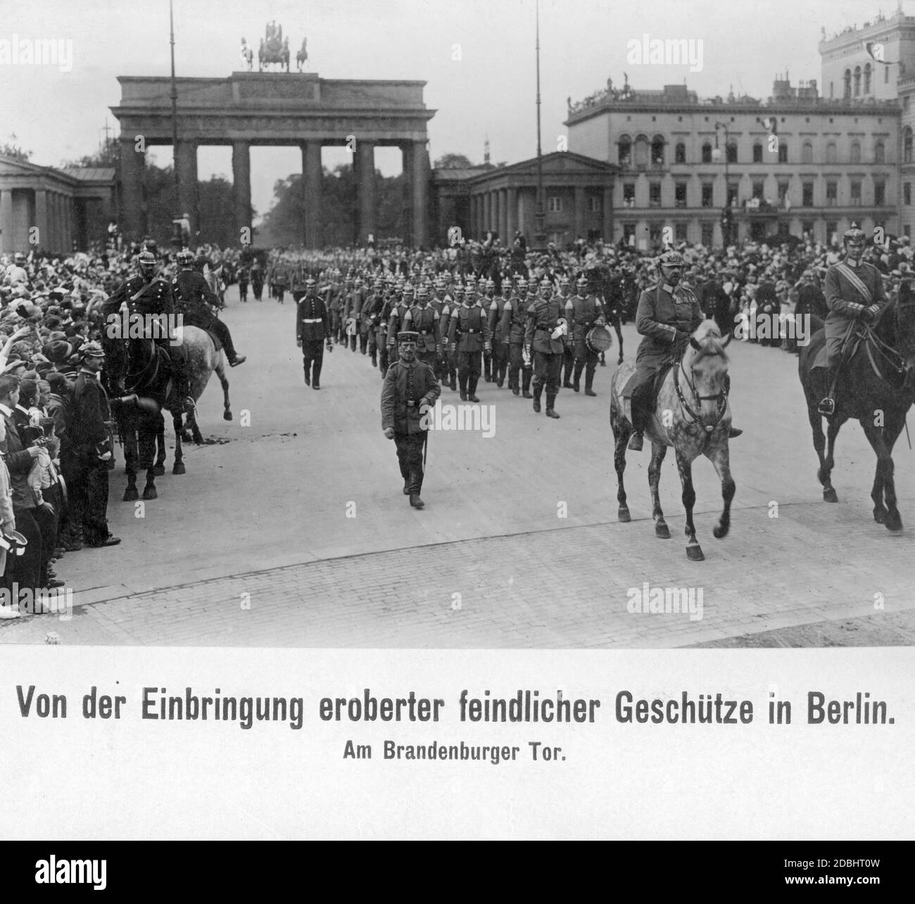 Bei einer Militärparade im September 1914 wurden vor dem Brandenburger Tor in Berlin gegnerische Geschütze präsentiert, die während des Krieges gefangen genommen wurden. Das Bild zeigt eine Menschenmenge, die die Parade einer Marschkapelle beobachtet. Zwei Offiziere reiten vorne. Stockfoto