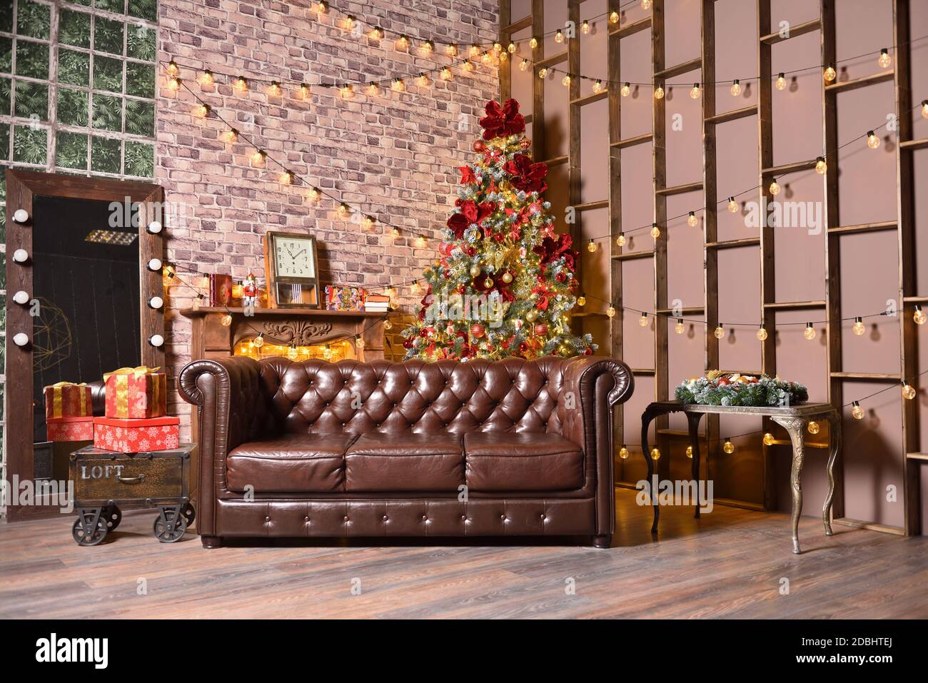 Stilvolle weihnachtsdekorationen im braunen Wohnzimmer mit Sofa, weihnachtsbaum und Girlanden an der Wand Stockfoto