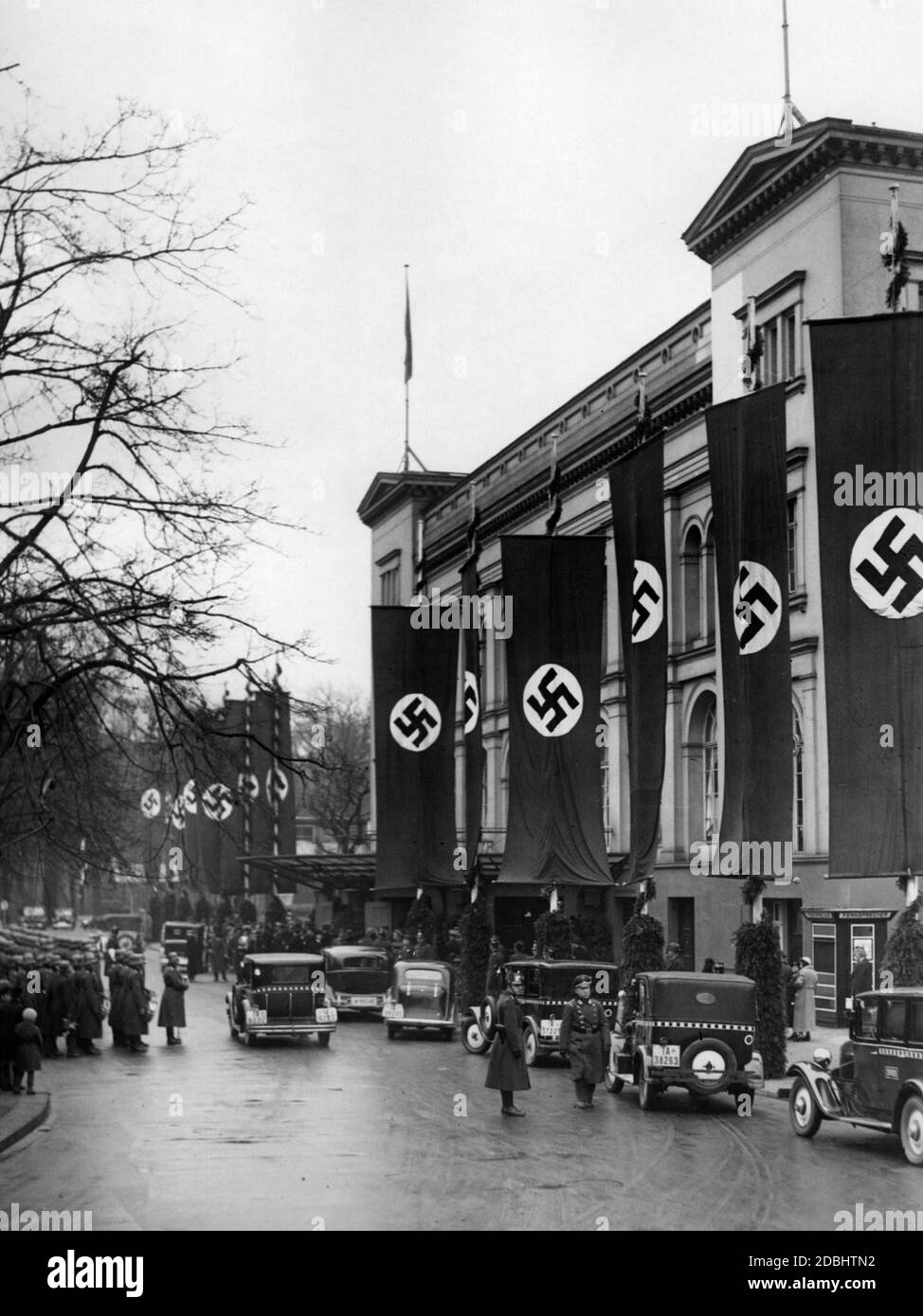 Blick auf das mit Hakenkreuzfahnen geschmückte Gebäude der Kroll-Oper anlässlich der Begrüßung der saarländischen Delegation durch Joseph Goebbels. Auf der linken Seite sind Soldaten der Wehrmacht, auf der rechten Seite sind mehrere Taxis. Stockfoto