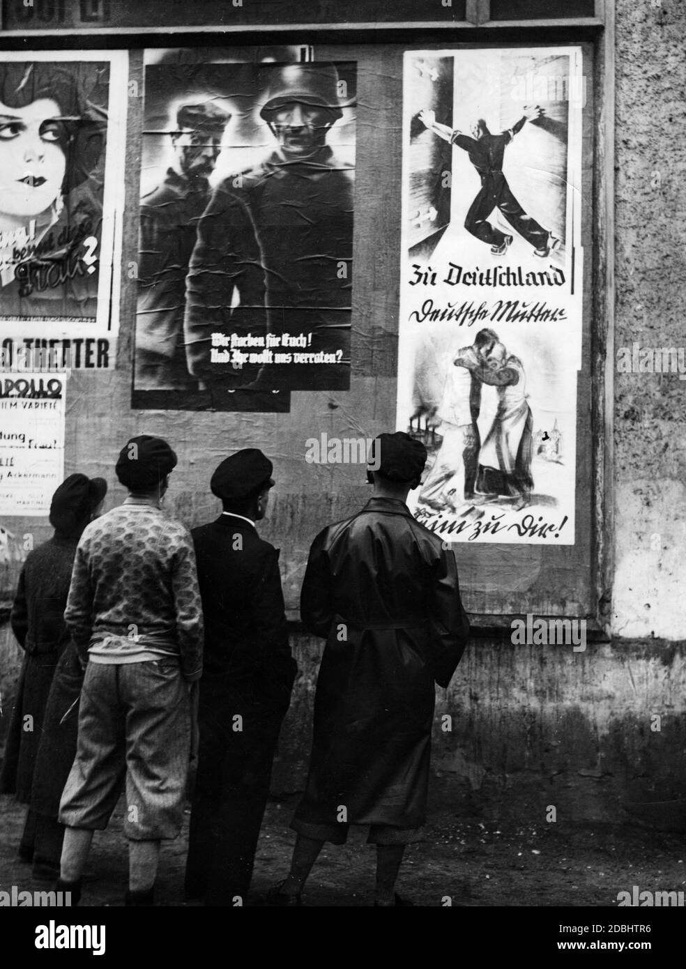 "Passanten schauen sich Wahlplakate an, die an einer Hauswand für das Referendum über die Annektierung der Saar an das Deutsche Reich hängen. Auf der linken Seite zwei Soldaten und die Inschrift: ''Wir sind für Sie gestorben! Und du willst uns verraten?''. Rechts: ''nach Deutschland'' und ''Deutsche Mutter. Home to You!''' Stockfoto