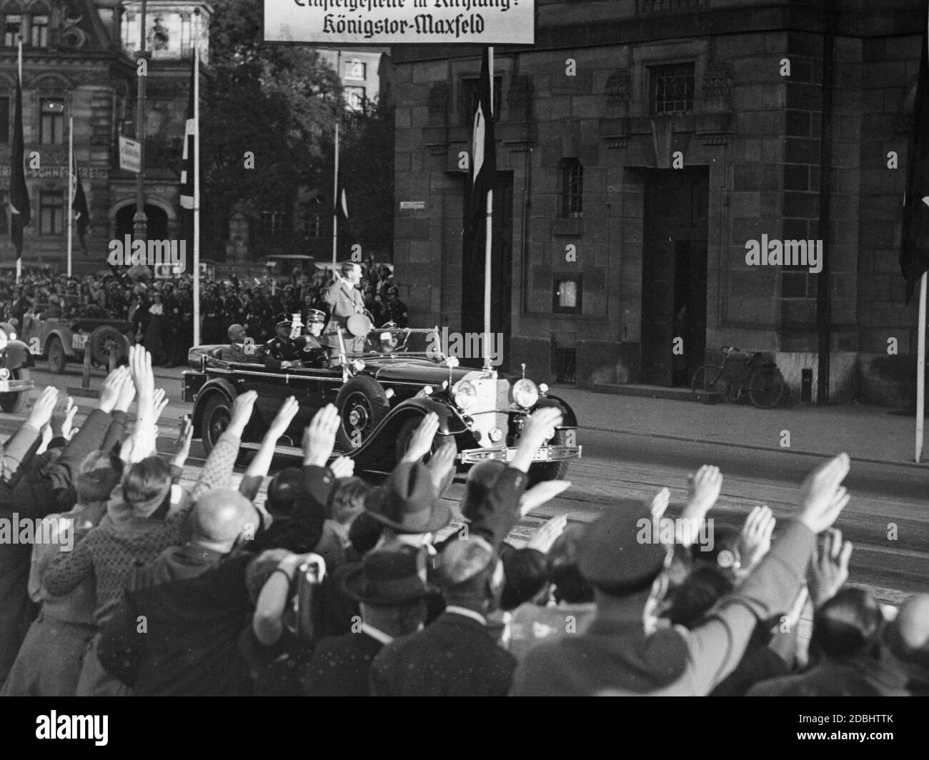 "Adolf Hitler wird in einem Mercedes mit Julius Schaub hinter sich sitzen, von den begeisterten Nürnberger begrüßt und fährt zum Hotel Deutscher Hof, wo er während des NSDAP-Kongresses in Nürnberg wohnen wird. Oben ist ein Schild mit der Aufschrift ''Boarding Point in Direction: Koenigstor-Maxfeld'''. Stockfoto