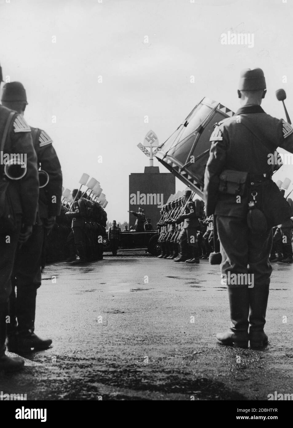 Adolf Hitler in einem Mercedes auf dem Zeppelin-Feld, nimmt den Gruß der etwa 50,000 Männer des Reichsarbeitsdienstes. Im Vordergrund steht eine Musikband mit Trommeln und Blasinstrumenten. Hinter Hitler, das Denkmal der Arbeit, an dem fand die Erinnerung an die Toten. Stockfoto