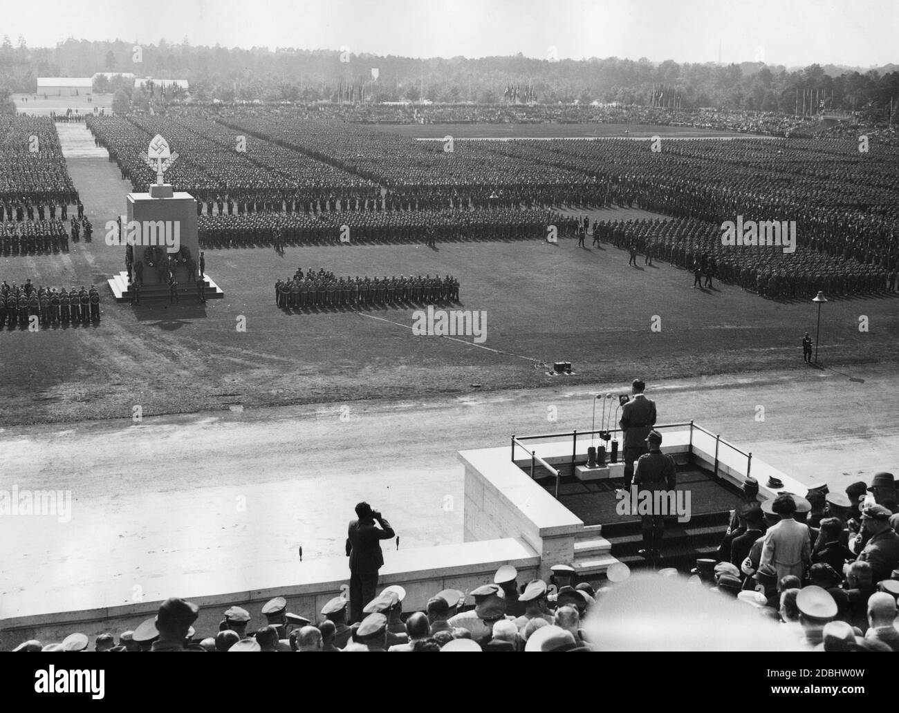 Adolf Hitler hält eine Rede vor den 54,000 Männern des Reichsarbeitsdienstes auf dem Zeppelinfeld. Hinter ihm steht Konstantin Hierl, links macht Heinrich Hoffmann ein Foto. In der Mitte des Platzes befindet sich das Denkmal der Arbeit, wo das Gedenken an die Toten abgehalten wurde. Stockfoto