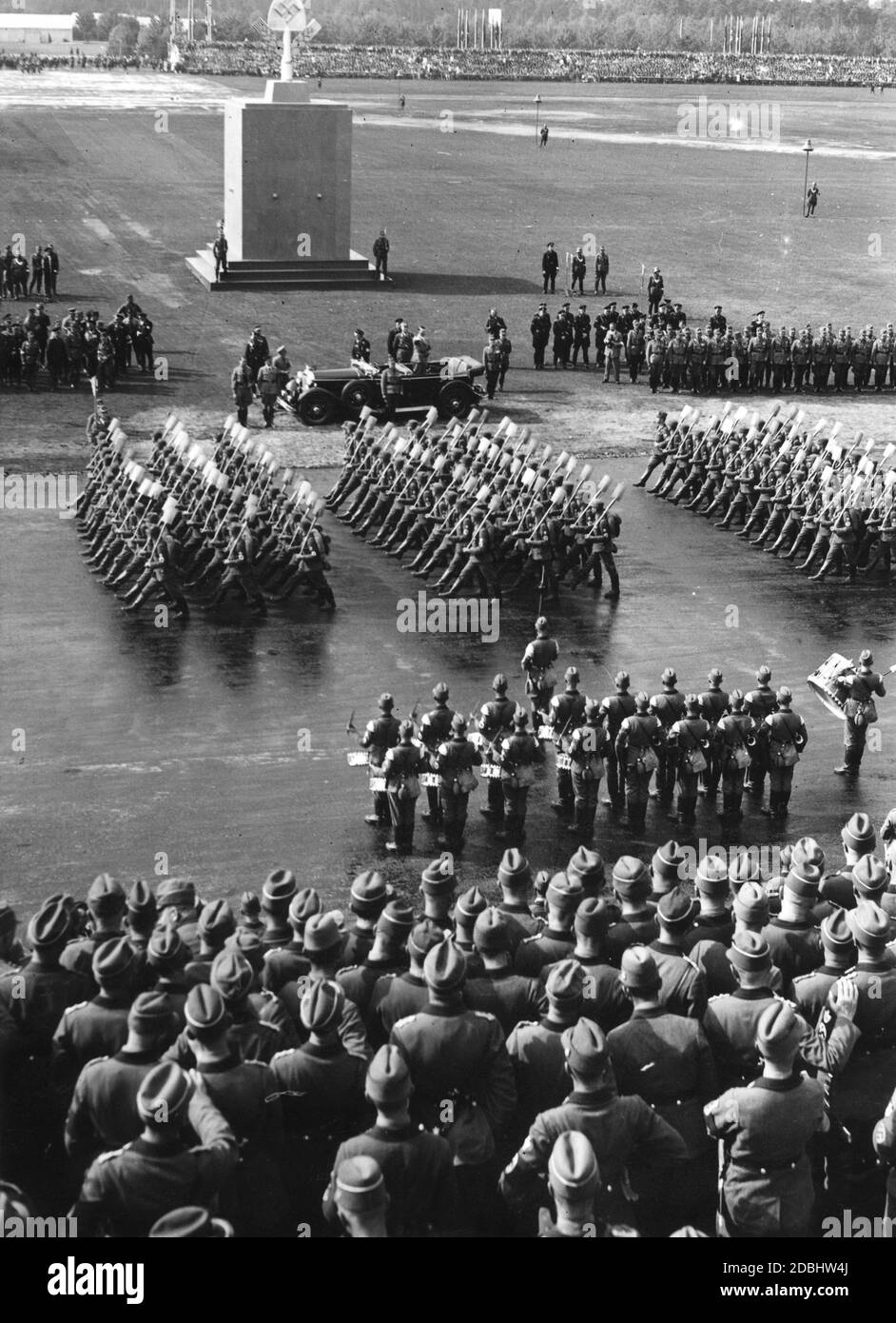 Adolf Hitler, im Mercedes stehend, (hinter ihm Wilhelm Brückner) grüßt die Formationen des Reichsarbeitsdienstes auf dem Zeppelinfeld. Im Hintergrund befindet sich das Denkmal der Arbeit, wo das Gedenken an die Toten stattfand. Im Vordergrund ist eine Gruppe von Trommlern. Stockfoto
