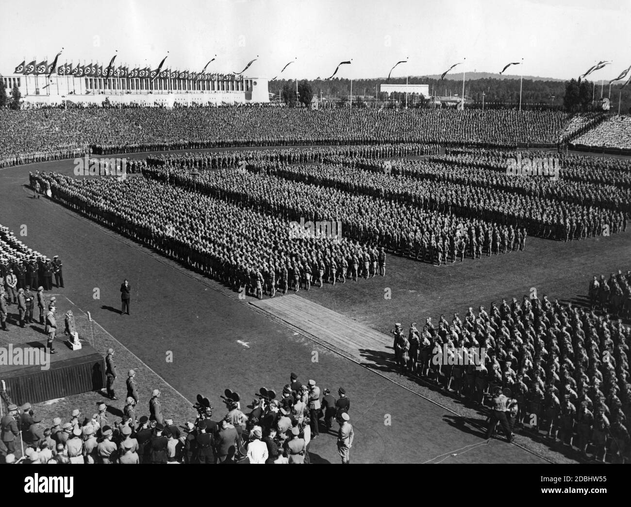 "Adolf Hitler, links auf der Rednerplattform, hält eine Rede im Stadtstadion vor den Teilnehmern des 'Tag der Hitlerjugend'. Links vom Rednerpult befindet sich der Marine-HJ. Vor ihm auf der Tartanbahn der Fotograf Heinrich Hoffmann. Auf der rechten Seite ein Kamerateam." Stockfoto
