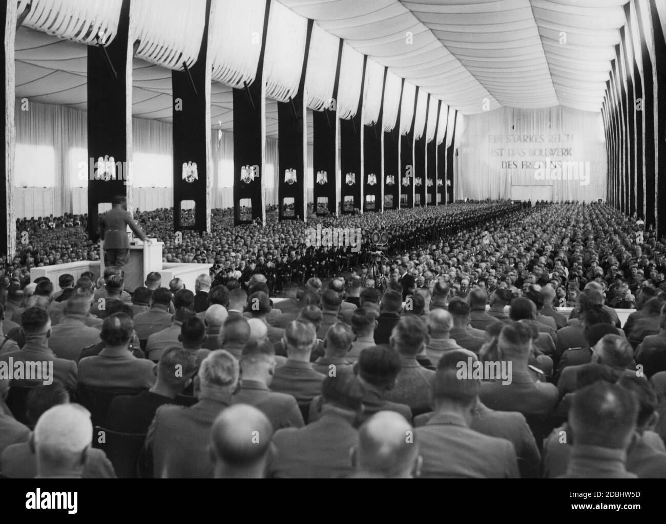 "Adolf Hitler hält eine Rede in der Luitpoldhalle auf der Konferenz der Deutschen Arbeiterfront. Auf der gegenüberliegenden Seite ist die Inschrift: "EIN starkes Reich ist das Bollwerk des Friedens". Auf der rechten Seite ist eine Filmkamera." Stockfoto