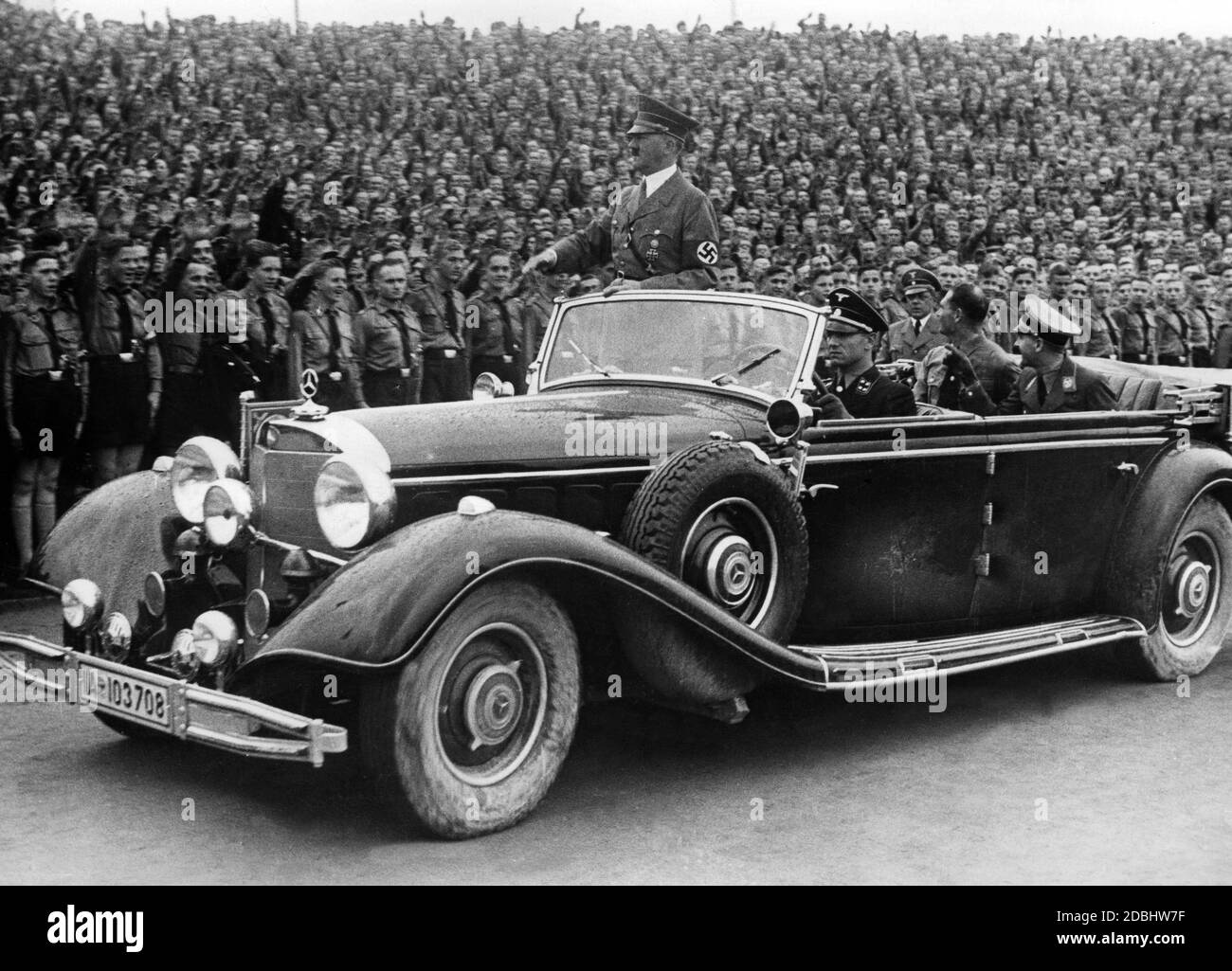 Adolf Hitler wird in einem Mercedes von Mitgliedern der Hitlerjugend und des BDM im Hitler-Jugendstadion begrüßt. Rudolf Hess und Baldur von Schirach sitzen auf dem Rücksitz. Links neben Hess befindet sich der Fotograf Heinrich Hoffmann. Stockfoto