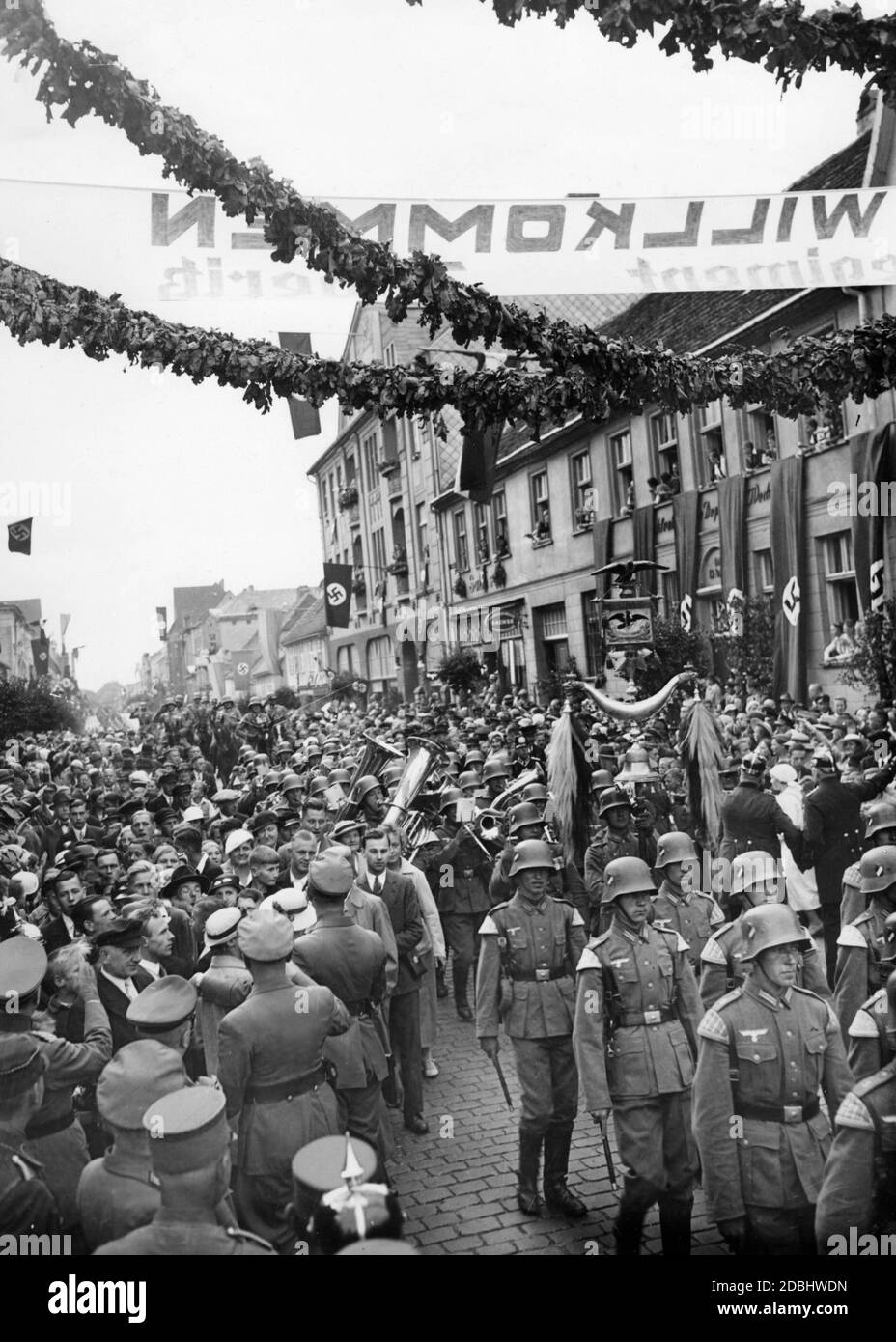 'Eintritt des Doeberitz-Regiments in Neustrelitz. Das Bild zeigt Zuschauer, marschierende Soldaten der Wehrmacht mit Pfeifen und Trompeten, Hakenkreuzfahnen und einem Banner mit der Aufschrift "Willkommen". Stockfoto