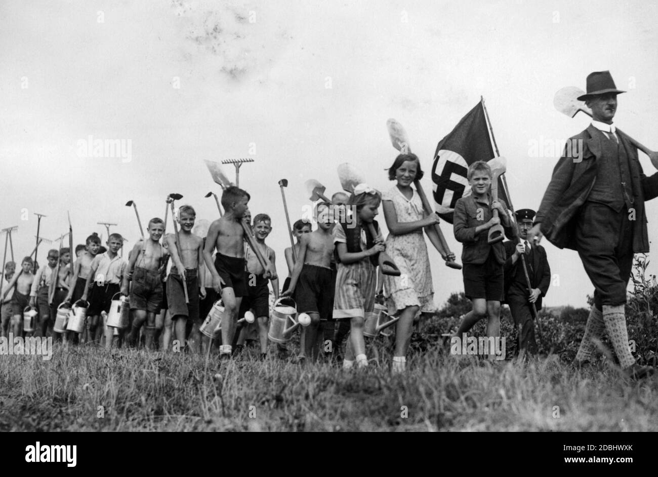 Eine Berliner Volksschulklasse, angeführt von ihrem Lehrer, ist auf dem Weg in den Schulgarten, ausgestattet mit Rechen, Gießkannen, Schaufeln und anderen Gartengeräten. Stockfoto