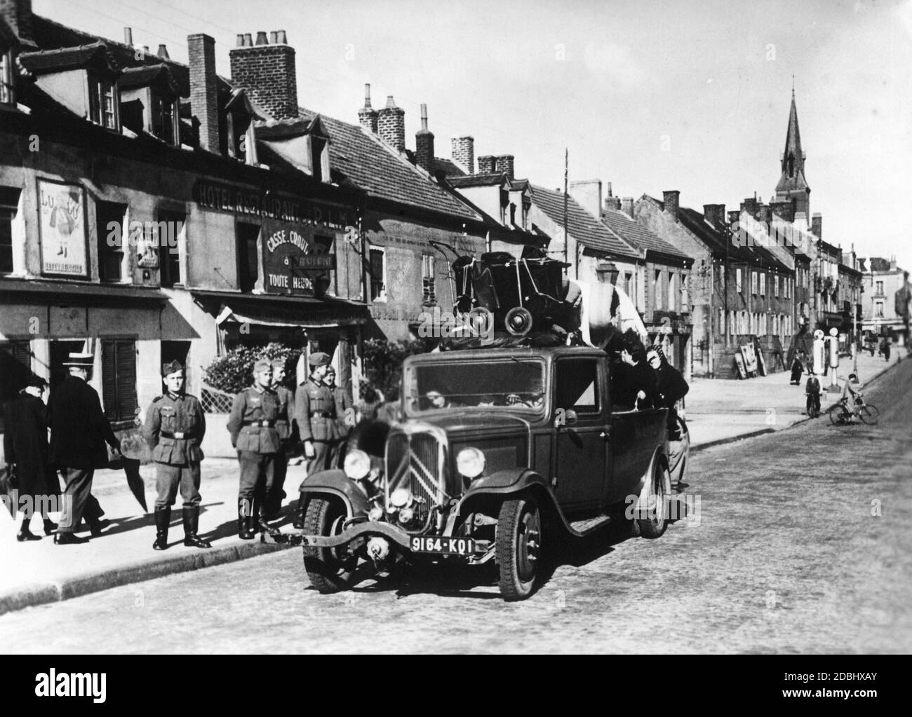 Rückkehr von Flüchtlingen nach Le Creusot in Bourgogne. Ein voll beladenes Fahrzeug steht in einer Straße vor einer Häuserzeile. Soldaten am Straßenrand. Stockfoto