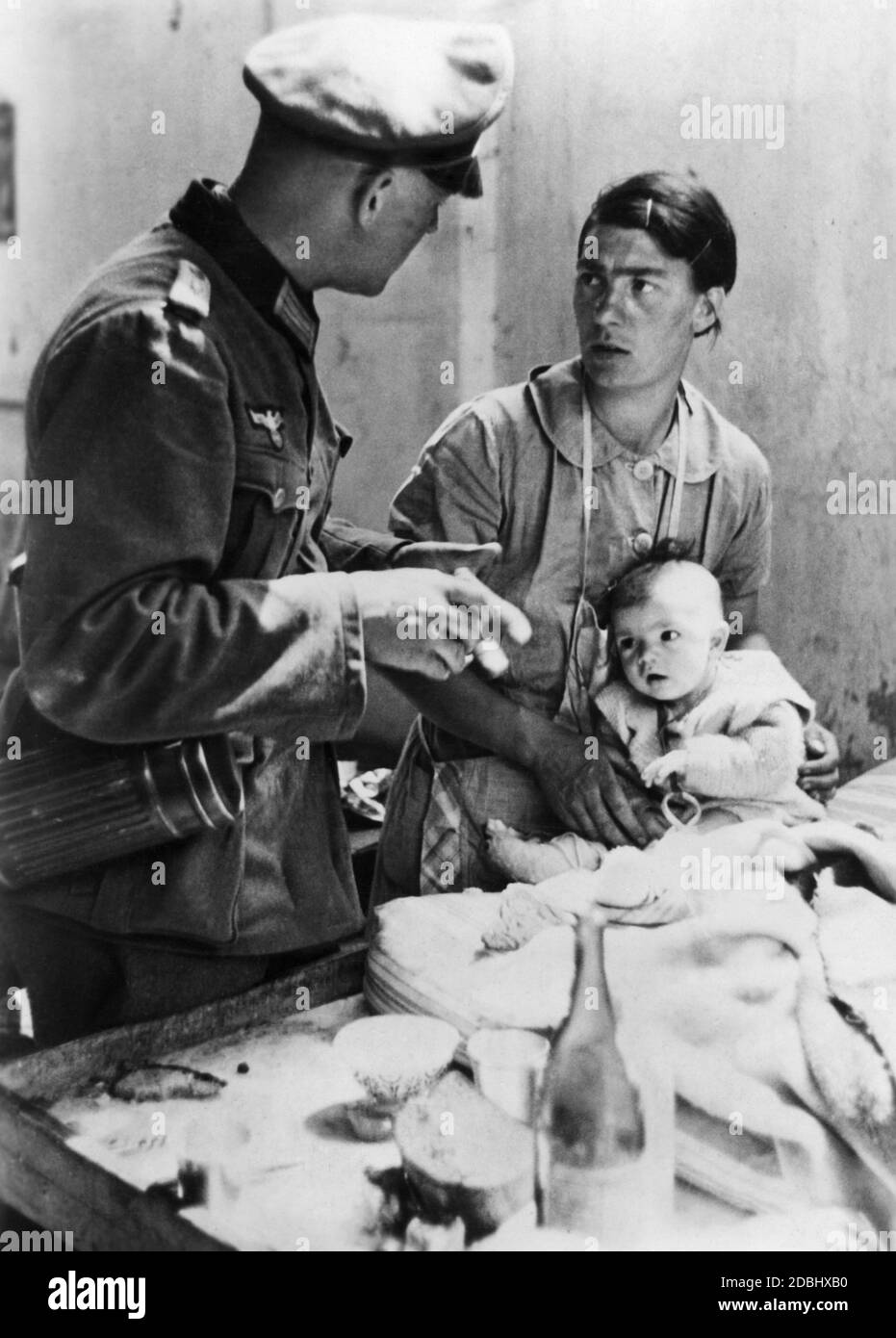 Ein Militärarzt kümmert sich um eine französische Frau, die ihr Baby in den Armen hält. Stockfoto