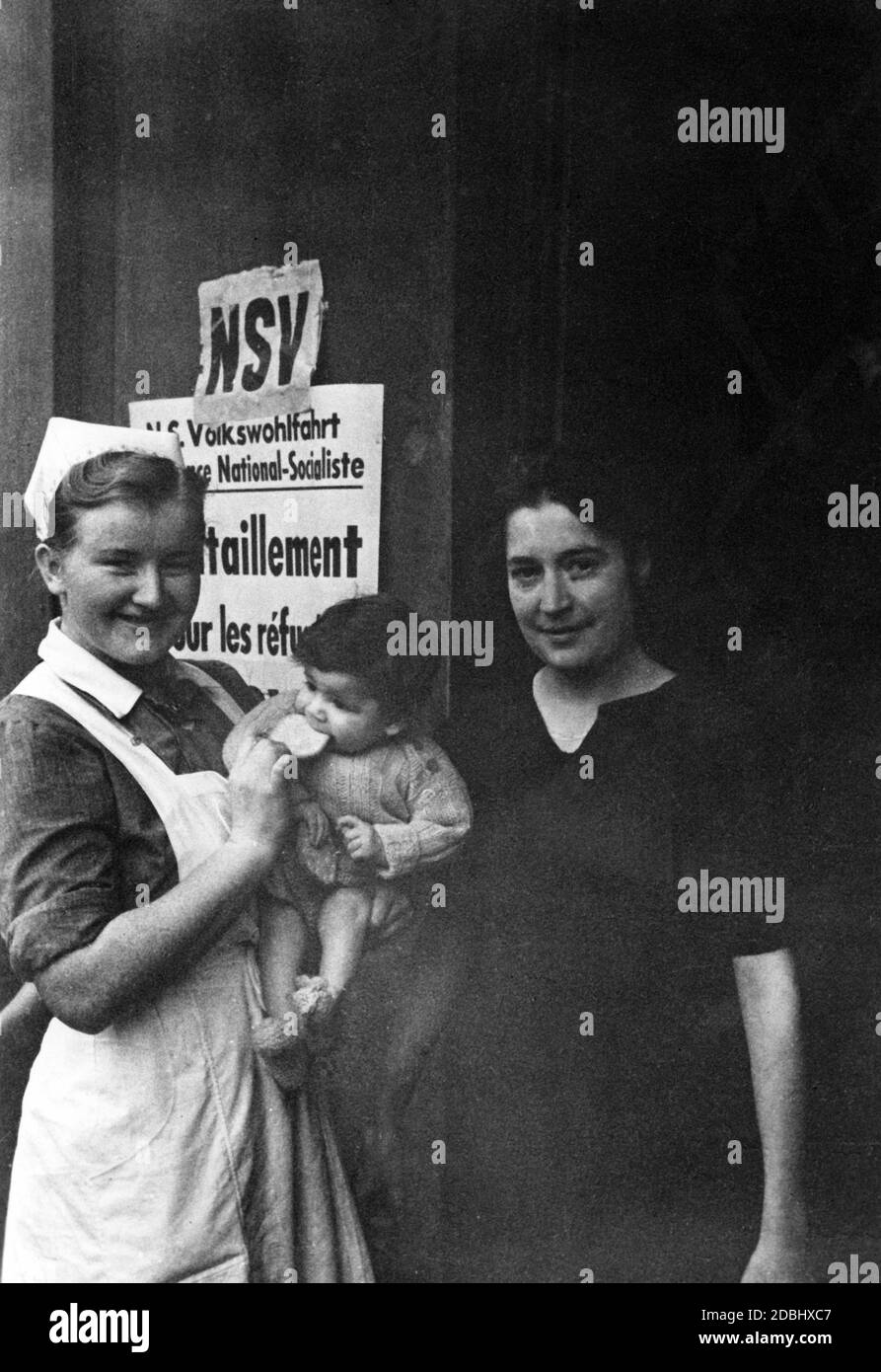 Ein Freiwilliger der NSV (National Socialist People's Welfare Organization) hält ein Kind in den Armen und ernährt es. Neben ihr ist wahrscheinlich die Mutter des Kindes. Stockfoto