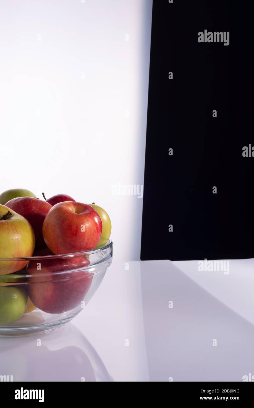 Satz von verschiedenen Sorten von Äpfeln in einem transparenten Glasbehälter. Auf einem schwarz-weißen Hintergrund Rote Äpfel in einem Teller auf weiß Stockfoto