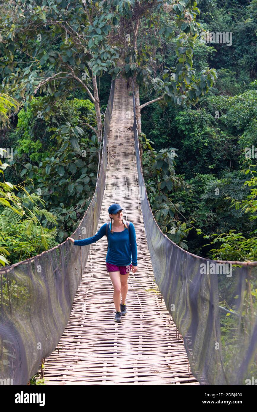 Eine Frau überquert eine prekär aussehende Hängebrücke über den Dschungel in Laos, Indochina, Südostasien, Asien Stockfoto