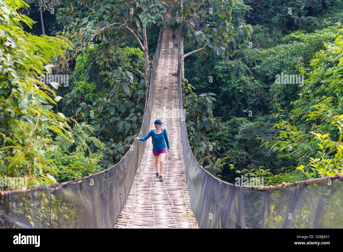 Eine Frau überquert eine prekär aussehende Hängebrücke über den Dschungel in Laos, Indochina, Südostasien, Asien Stockfoto