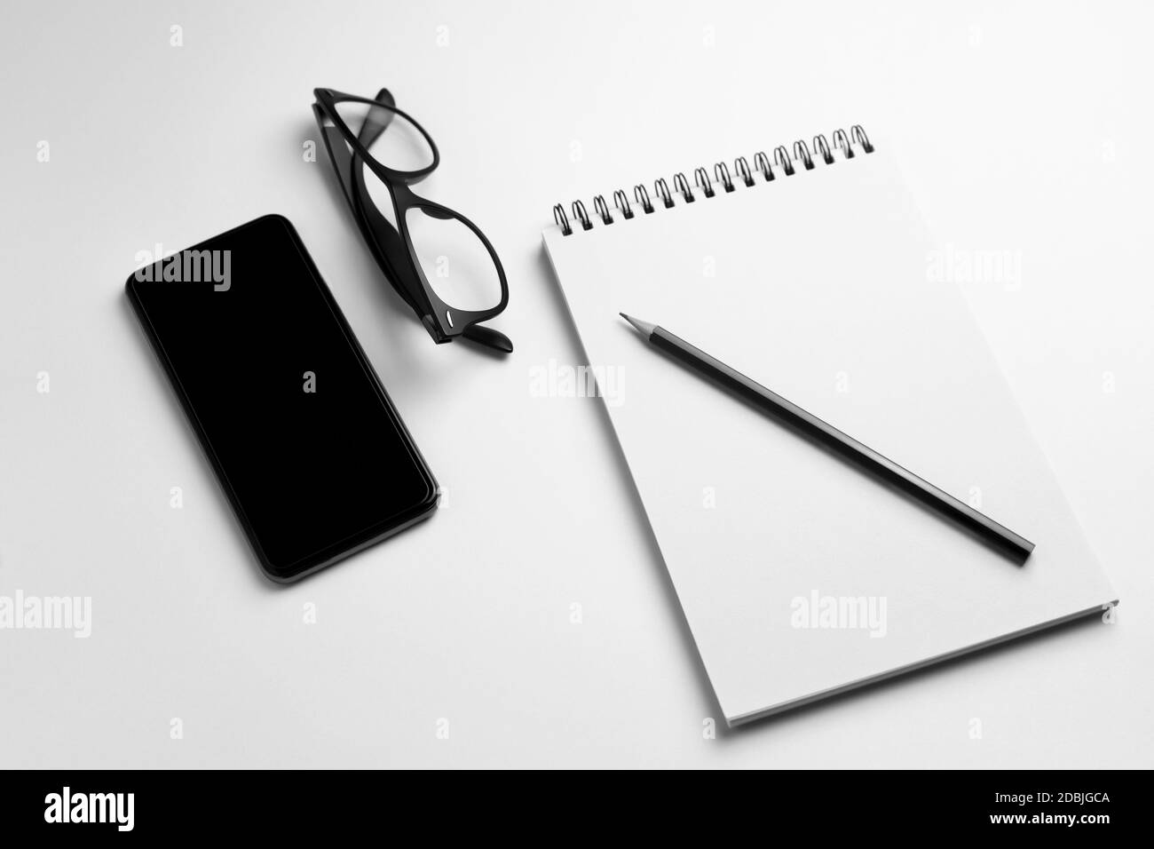 Smartphone mit leerem Notebook, Bleistift und Brille auf weißem Hintergrund.Draufsicht Konzept von Business, Arbeitsplatz und Technologie. Stockfoto