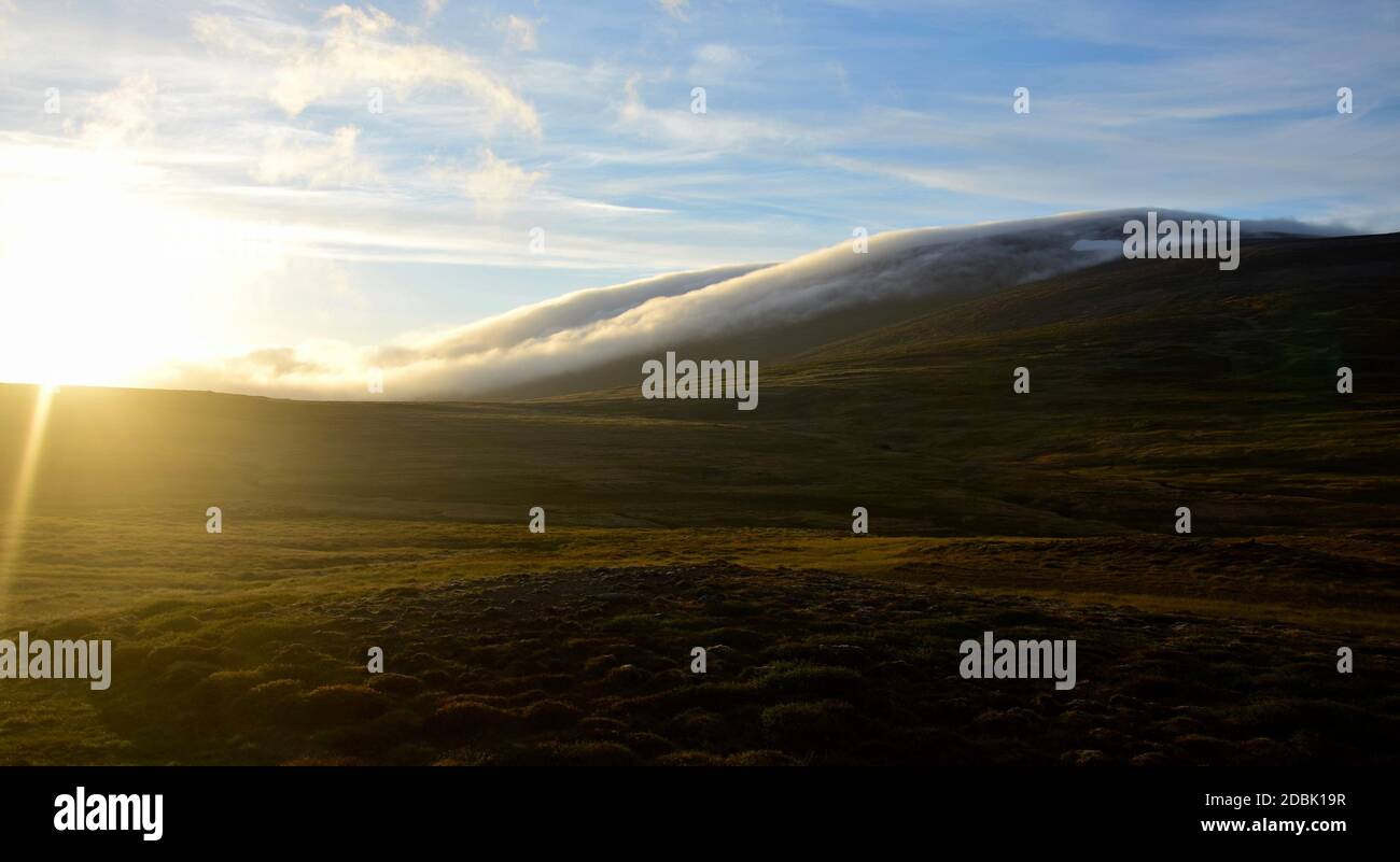 Eine Hochsommernacht in Island. Wolken treiben einen Berg hinunter. Contre-jour. Stockfoto