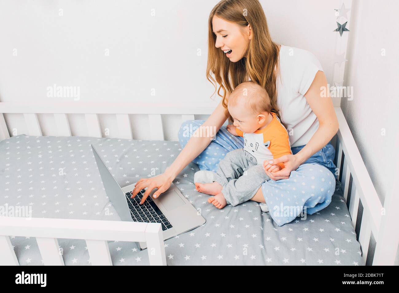 Eine junge Mutter im Schlafanzug mit einem kleinen Kind, sitzt auf dem  Bett, mit einem tragbaren Laptop. Das Konzept der Remote-Arbeit in  Quarantäne Stockfotografie - Alamy