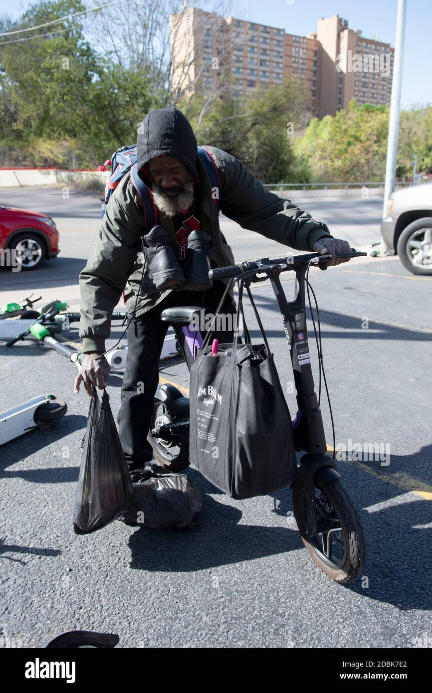 Ein Obdachloser benutzt einen Roller, um an der Ecke von East Cesar Chavez und Red River Street an einem Sonntagmorgen in der Innenstadt von Austin, TX, Taschen zu tragen. Die beliebte Art, Austin's Stadtkern zu erkunden, hat eine Reihe von urbane Gefahren hervorgebracht, nachdem viele Besucher sie nach einer Partynacht in der Rainey Street auf Gehwege werfen. Stockfoto