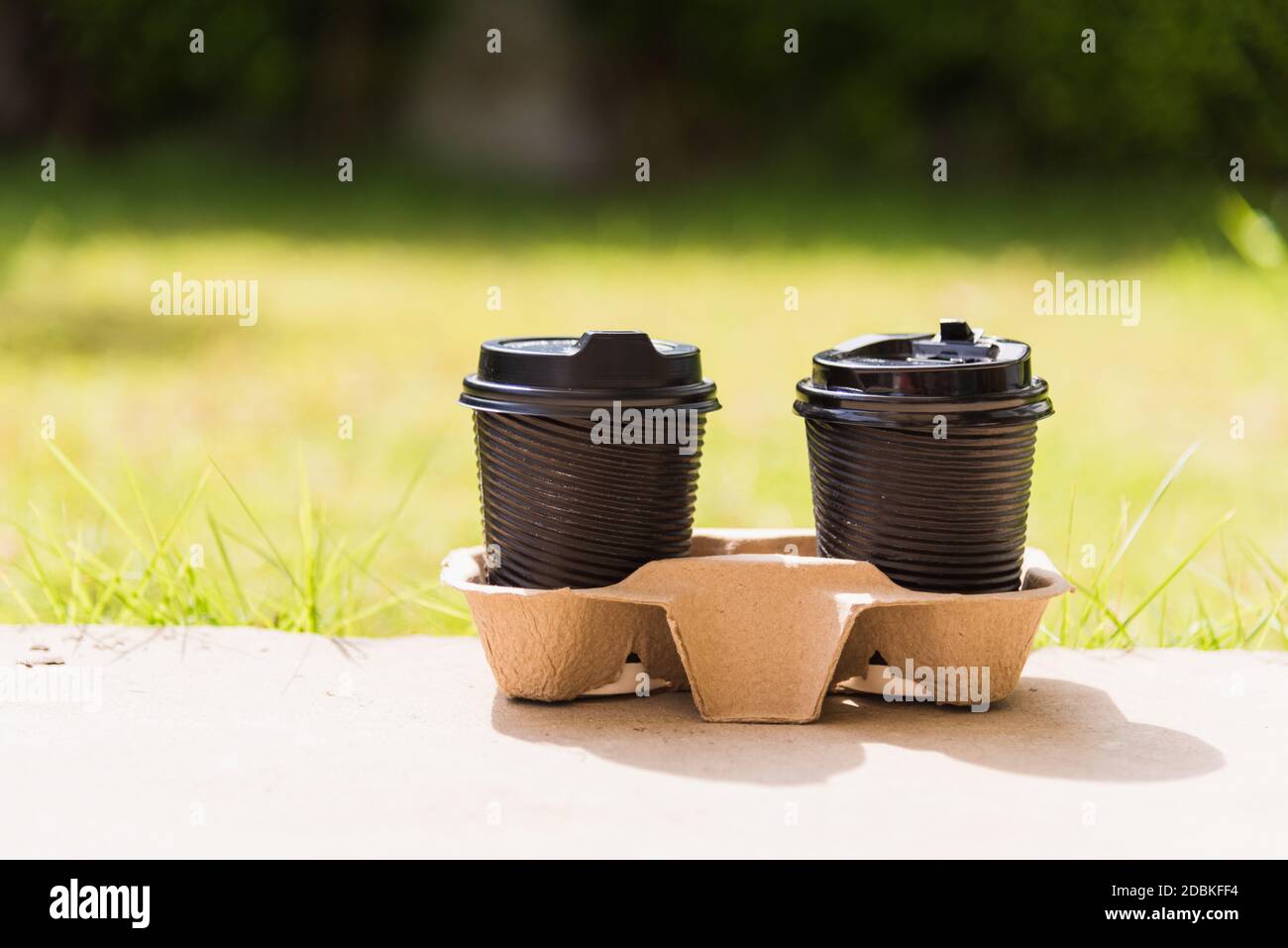 Nahaufnahme von zwei schwarzen Pappbecher heißen Kaffee zum Mitnehmen auf dem Boden außerhalb des Cafés auf dem Garten Platz der grünen Blätter Farbe Hintergrund für Kopie sp Stockfoto