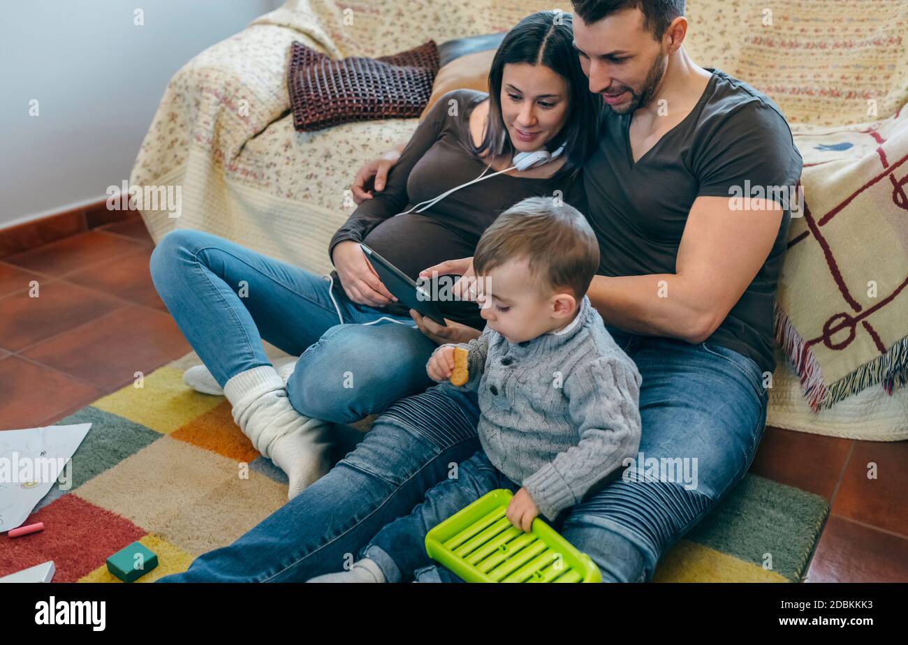 Schwangere Frau und Mann suchen Tablette, während Sohn spielt Stockfoto