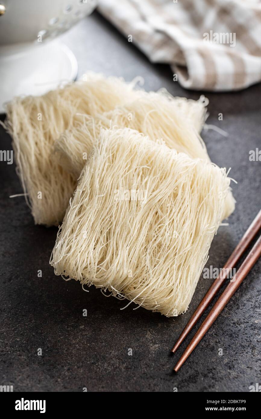 Ungekochte weiße Reisnudeln und Essstäbchen auf schwarzem Tisch. Stockfoto