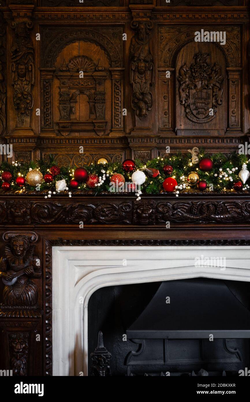 Ein schönes traditionelles Holzfeuer umgeben mit komplizierten Schnitzereien geschmückt mit einer festlichen Weihnachtsgirlande aus rot, grün und Gold. Stockfoto
