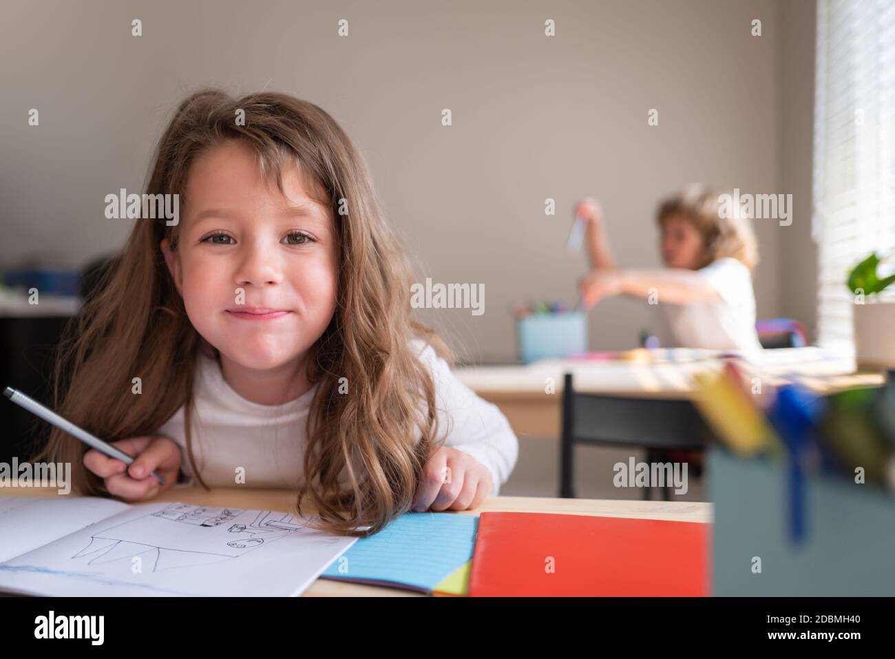 Lustige glücklich Schulmädchen schriftlich Notizen in der Klasse. Kinder im Klassenzimmer in der Schule. Schüler am Schreibtisch in der Grundschule mit Blick auf die Kamera. Stockfoto