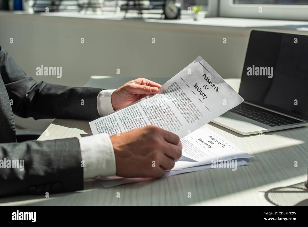 Beschnittene Ansicht des Geschäftsmannes, der Petition für Bankrott hält, während er am Arbeitsplatz auf verschwommenem Hintergrund sitzt Stockfoto