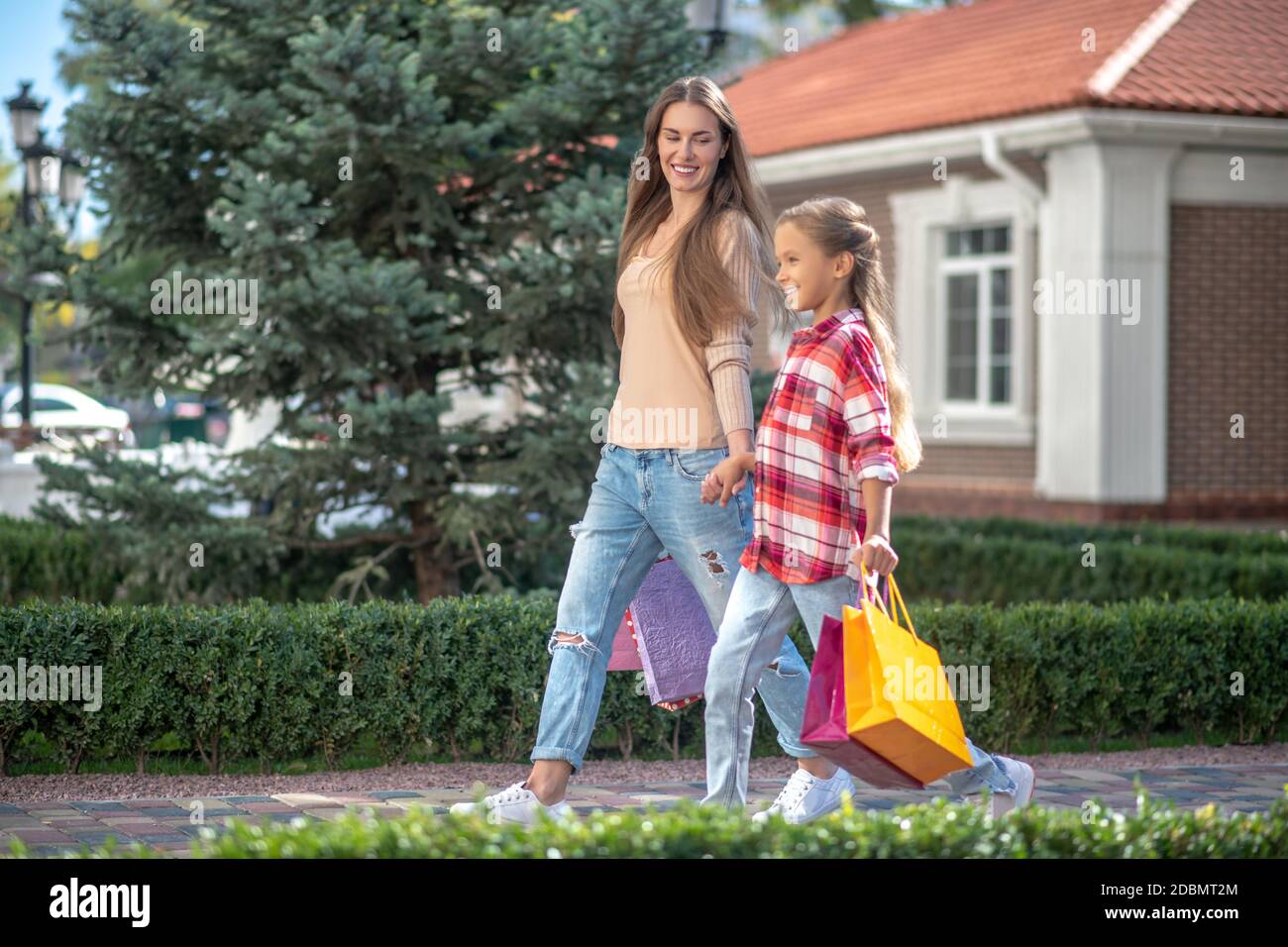 Lächelnde Mutter und Tochter gehen Hand in Hand mit Einkaufen Taschen Stockfoto