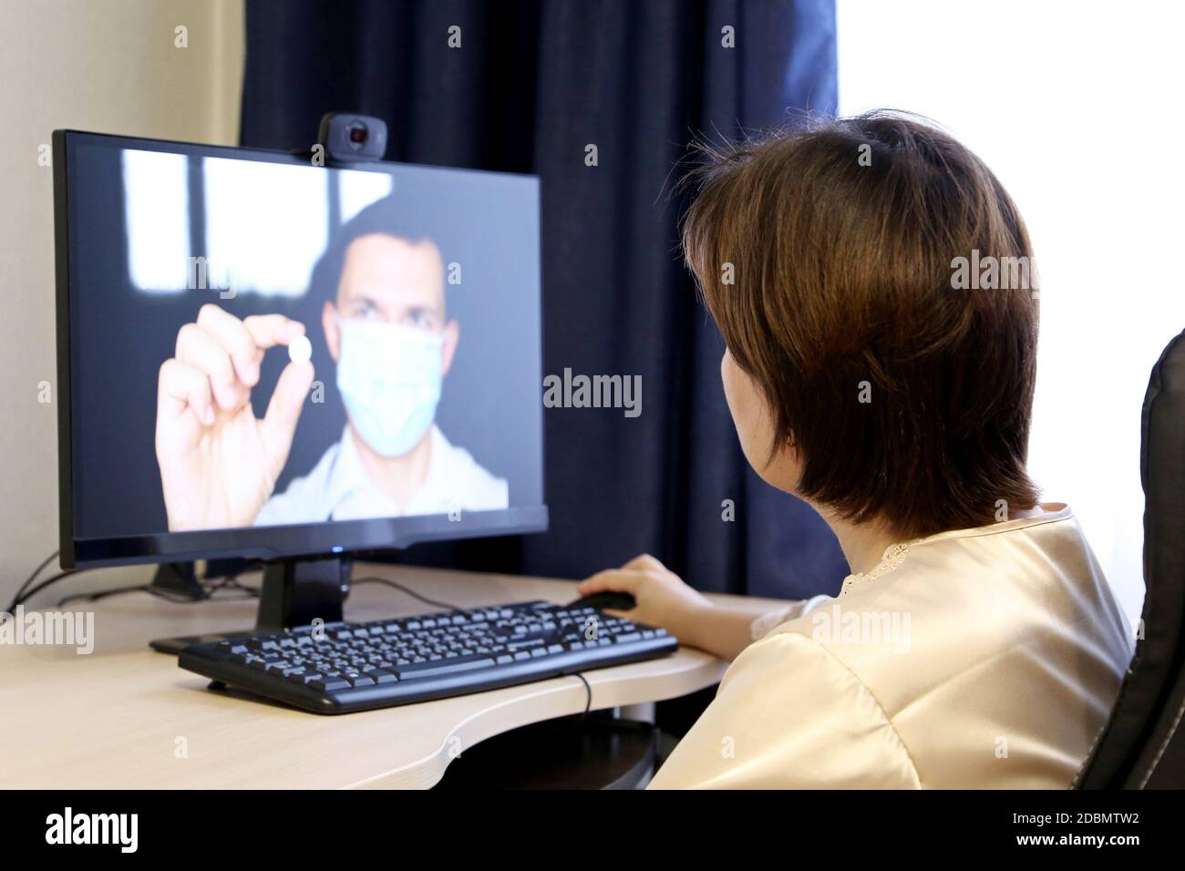 Online-Beratung mit einem Arzt, Frau hört sich die Arzt Empfehlungen sitzen vor der PC-Webcam. Mann in medizinischer Maske mit Pille Stockfoto