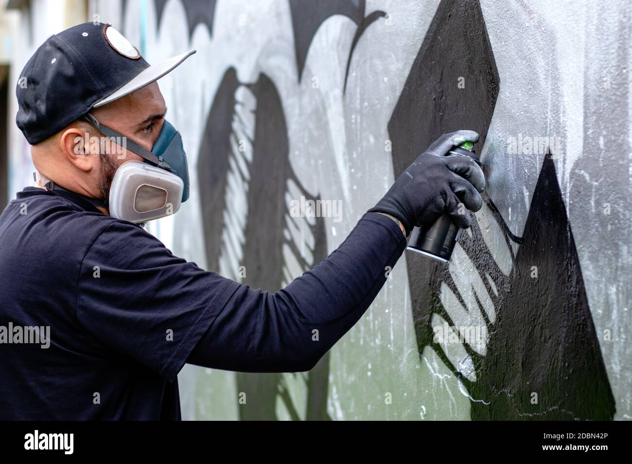 Graffiti-Künstler in Aktion, Zeichnung an der Wand mit Aerosol-Sprühfarbe  in einer Dose, tragen Schutzmaske / Atemschutzmaske mit Filtern.  Straßenkunst Stockfotografie - Alamy