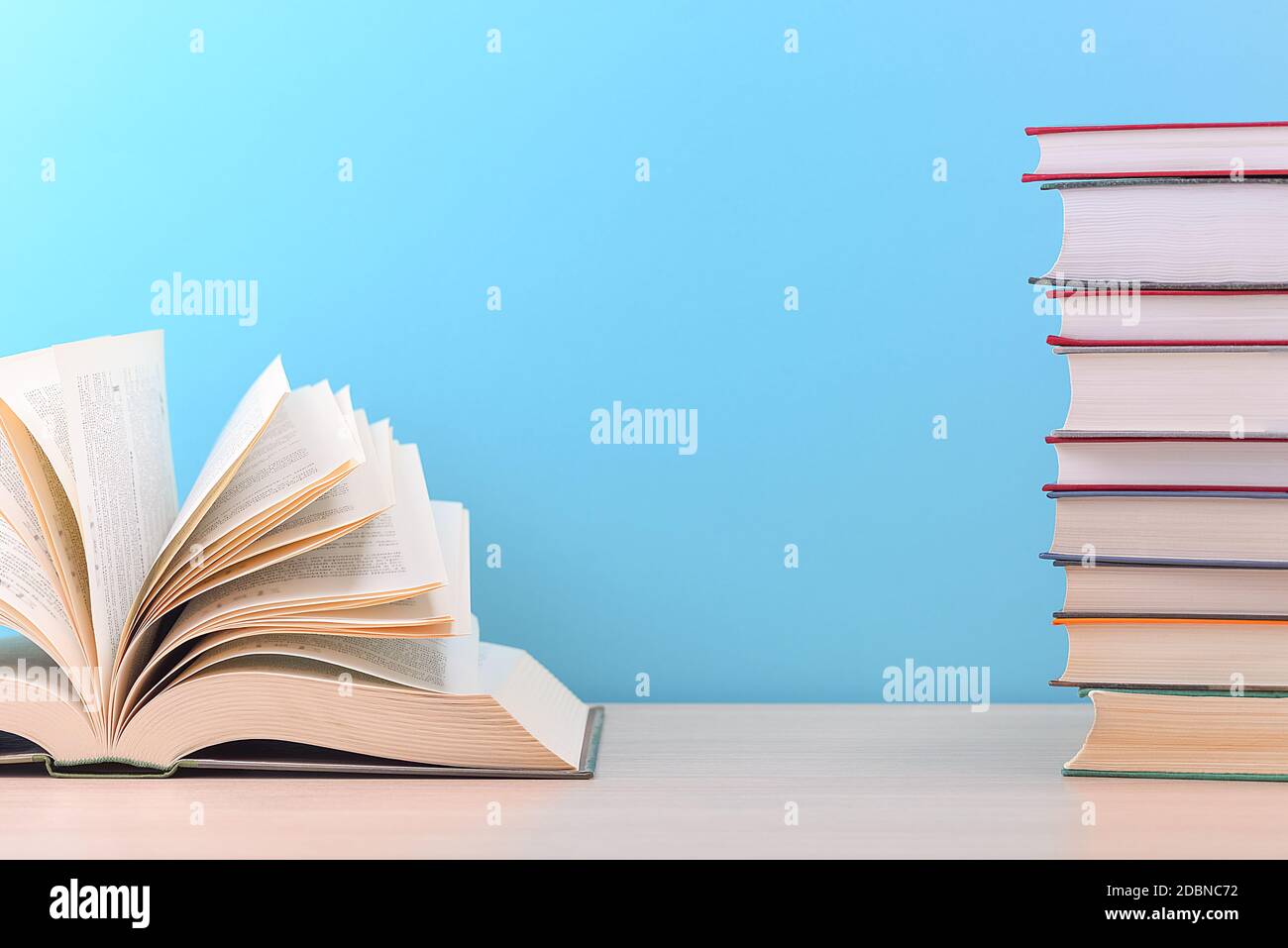 Ein großes, dickes Hardcover-Buch liegt auf einem hellen Holztisch. Das Buch ist offen, neben einem Stapel geschlossener Bücher, und auf der Rückseite ist ein blauer Hintergrund Stockfoto