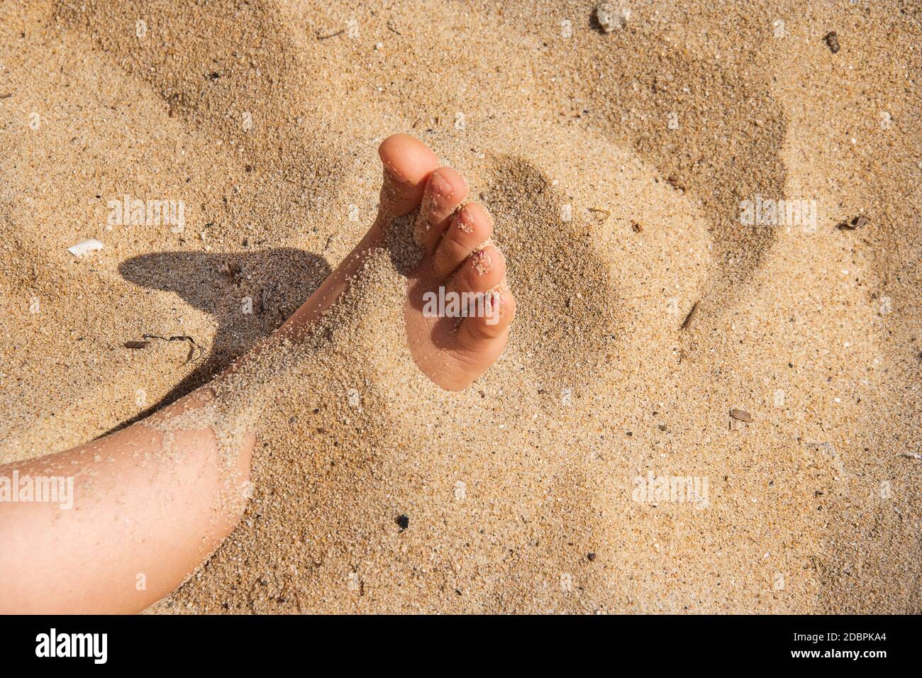 Fuß im Sand. Kind menschlichen nackten Füßen in der Meeresfotografie begraben. Zehe versteckt im Sand. Mädchen spielt am Strand und versteckt sie barfuß. J Stockfoto