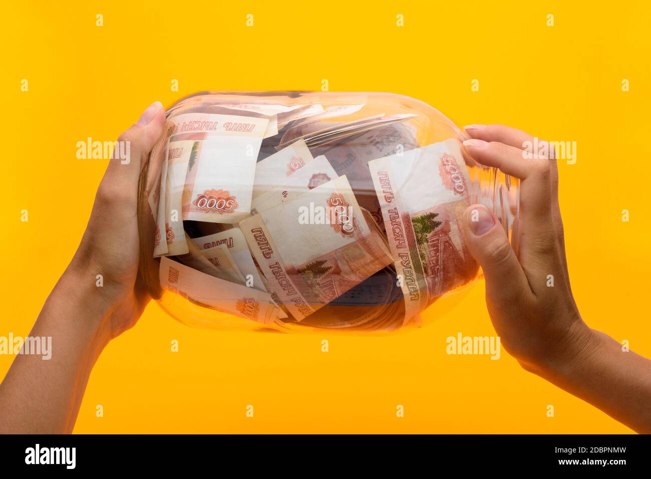Hände halten ein drei-Liter-Glas, in dem liegen fünftausend Scheine, gelber Hintergrund Stockfoto