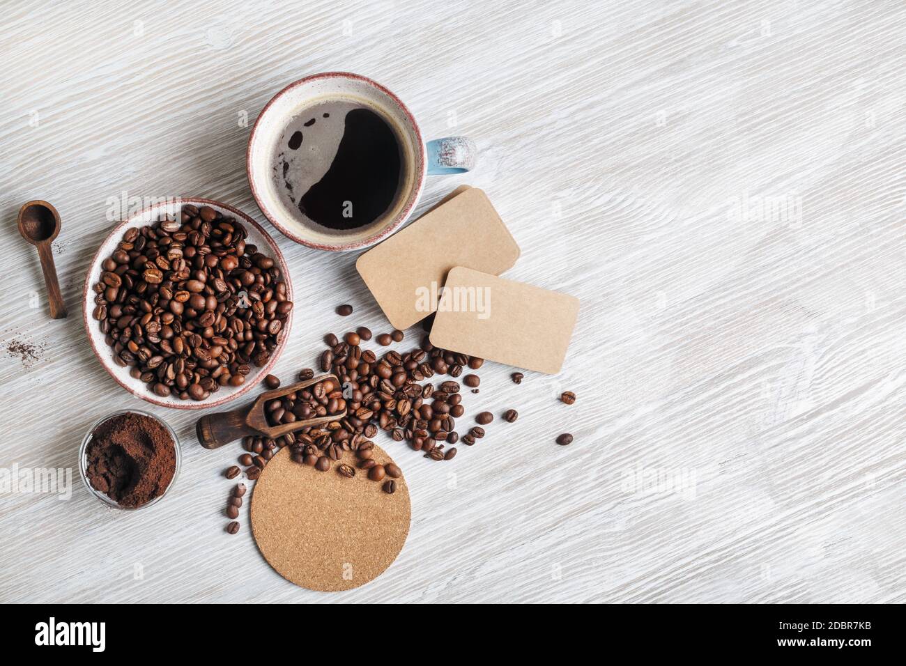 Foto von frischem leckeren Kaffee auf hellem Holz Küchentisch. Kaffeetasse, Kaffeebohnen, gemahlenes Pulver, Bierdeckel und leere Kraft Visitenkarten. .Flat l Stockfoto