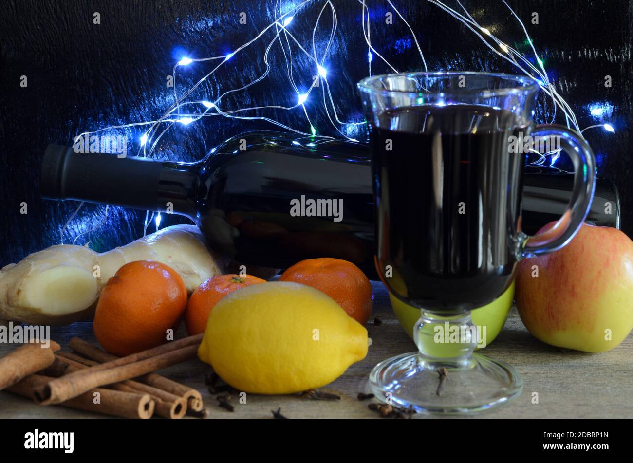 Eine Flasche Rotwein. Ein Glas Glühwein, Ingwerwurzel, Zimtpfeifen, Nelken, Apfel und Mandarinen auf verschwommenem Hintergrund. Selektiver Fokus. Stockfoto