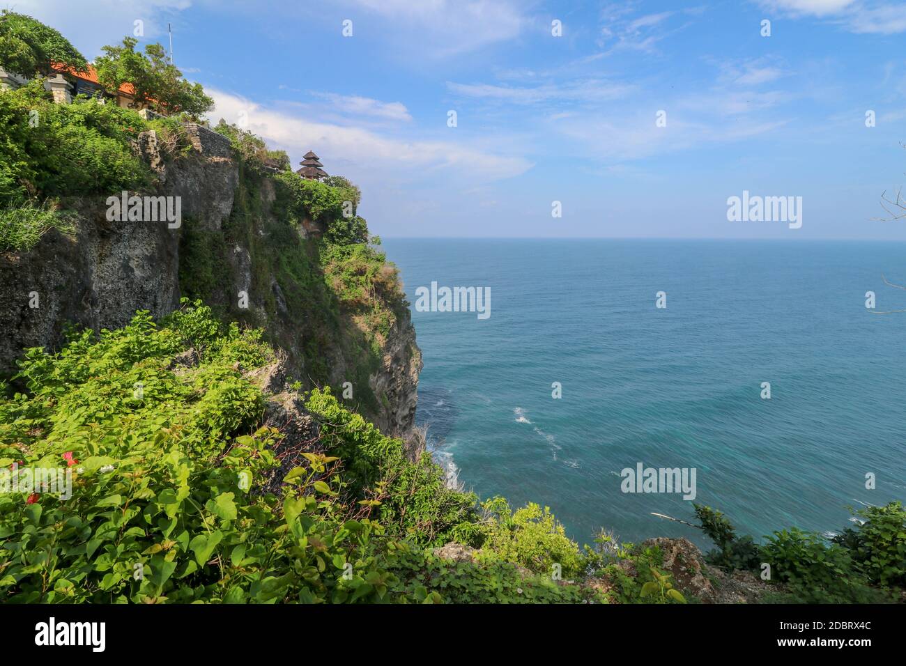 Blick auf Uluwatu Klippe mit Pavillon und blauem Meer in Bali, Indonesien. Schöne Landschaft von Pura Luhur Uluwatu Tempel mit bunten Blumen im Vordergrund d Stockfoto